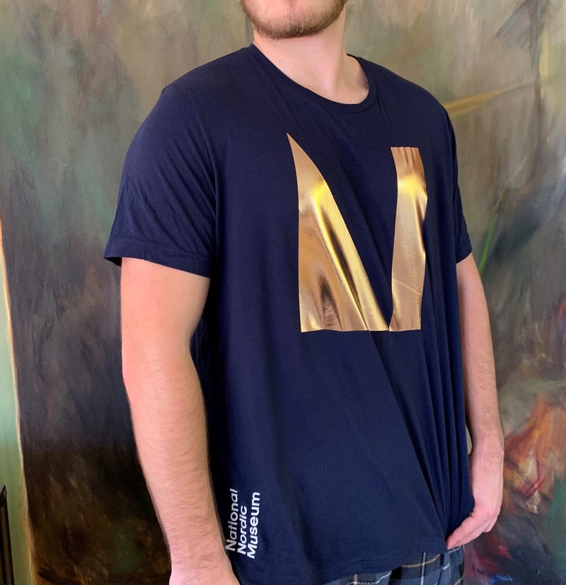 Show your pride in the National Nordic Museum by sporting this cute tee! Our newest poly cotton t-shirt comes in navy blue with a shimmery rose gold foil logo.