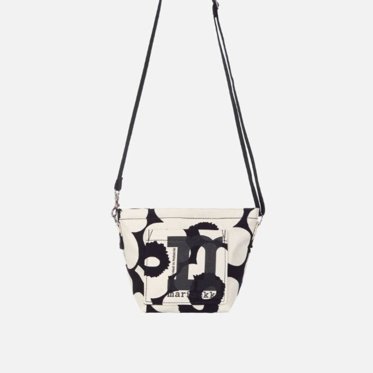 The Mono Mini Crossbody is made of unbleached organic cotton, which features the Unikko pattern printed in Helsinki. The shoulder bag has a zipper closure, an open pocket on the outside, and an adjustable shoulder strap.