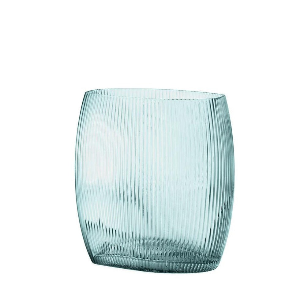 Normann Copenhagen -Tide Vase H18 cm Blue The raw nature of the Danish North Sea, with its strong winds and currents, has served as inspiration for the Tide vase. Its dynamic shape mimics the movement of waves while its grooved surface resembles ripples in the sand, creating a semi-transparent effect.